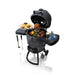 Broil King Keg 5000 kamado charcoal grill open with chicken, steaks, vegetables, corn, and accessories displayed on the cooking surface and side shelves.