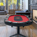 Triton 10 player folding poker table in a modern living room with red felt surface, black center area, padded rail, and cup holders.