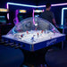 Hathaway Breakaway Dome Hockey table shown in an arcade setting with neon lights, focusing on the clear dome and blue table sides.