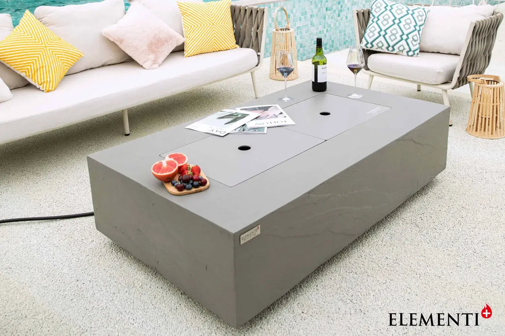 Functional detail of the Elementi Plus Meteora fire table used as an outdoor coffee table with the burner lid in place, styled with wine, champagne, and snacks.