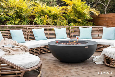 Modern outdoor patio featuring a gray concrete fire bowl with glass wind guard and curved outdoor sofa seating.
