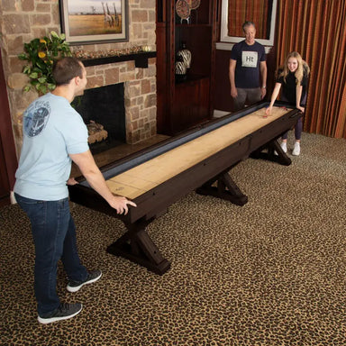 Three people enjoying the Freetime Fun Espresso Shuffleboard Table in a home game room setting.