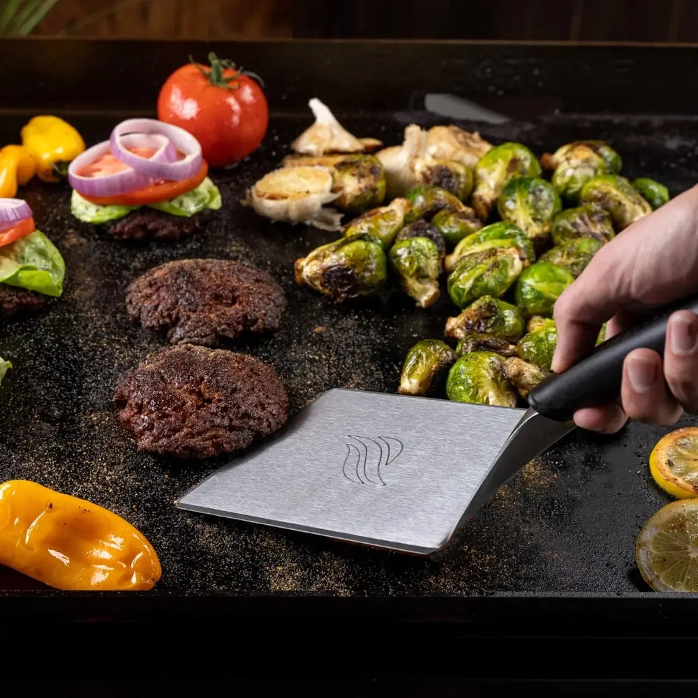 Blackstone burger spatula flipping patties and veggies on flat top griddle