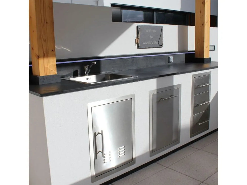 Sunstone 16" stainless trash drawer installed in outdoor kitchen island with sink, storage doors, and stone countertop.