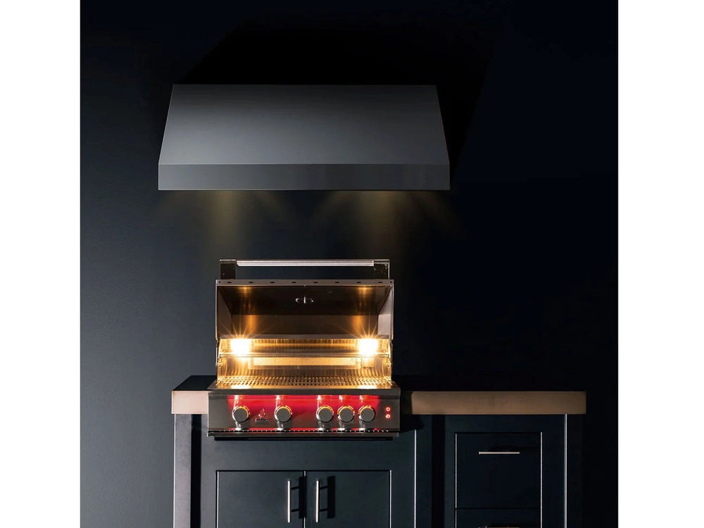 True Flame built-in grill illuminated at night under a vent hood in a sleek outdoor kitchen setup.
