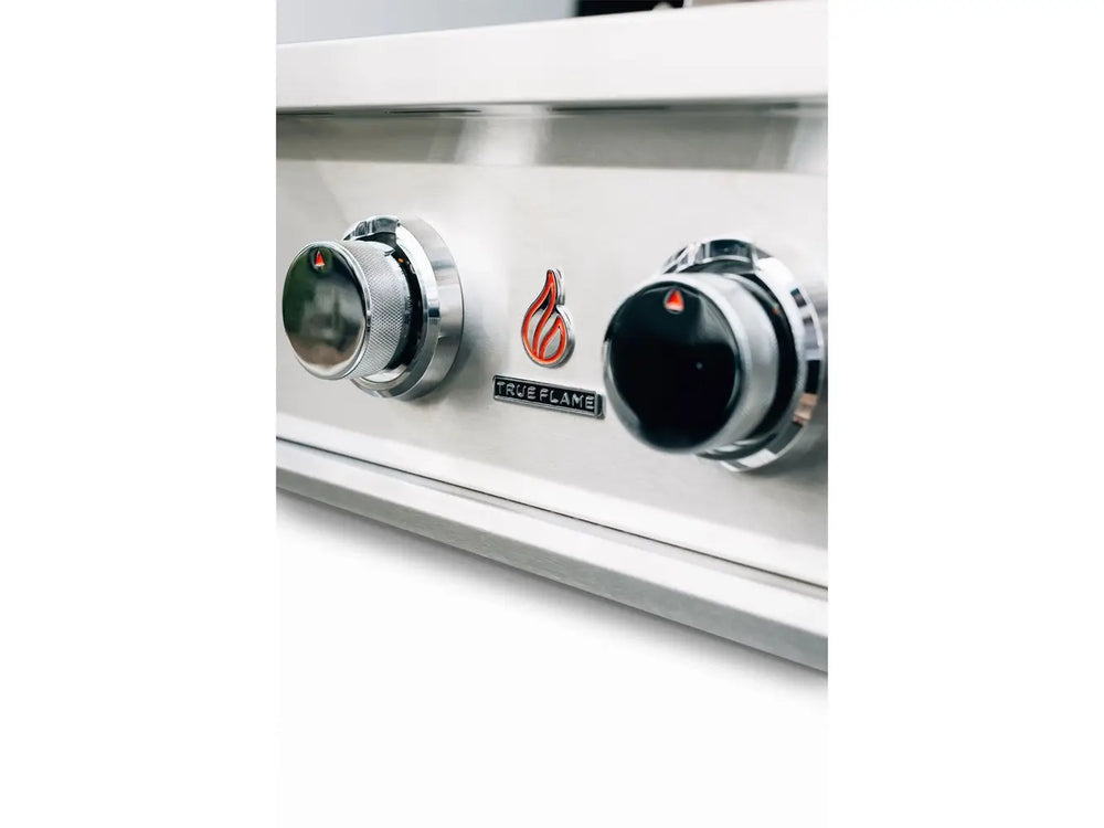 Macro view of True Flame gas grill control panel with chrome knobs and brand logo on stainless steel body.