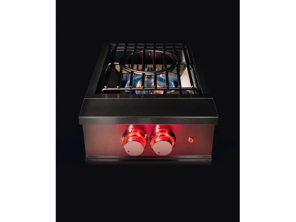Night view of True Flame wok burner in use with visible blue flames under stainless steel grates and glowing red knobs.