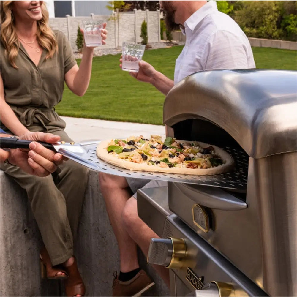 Family backyard setup with pizza oven on table and toppings arranged for outdoor cooking