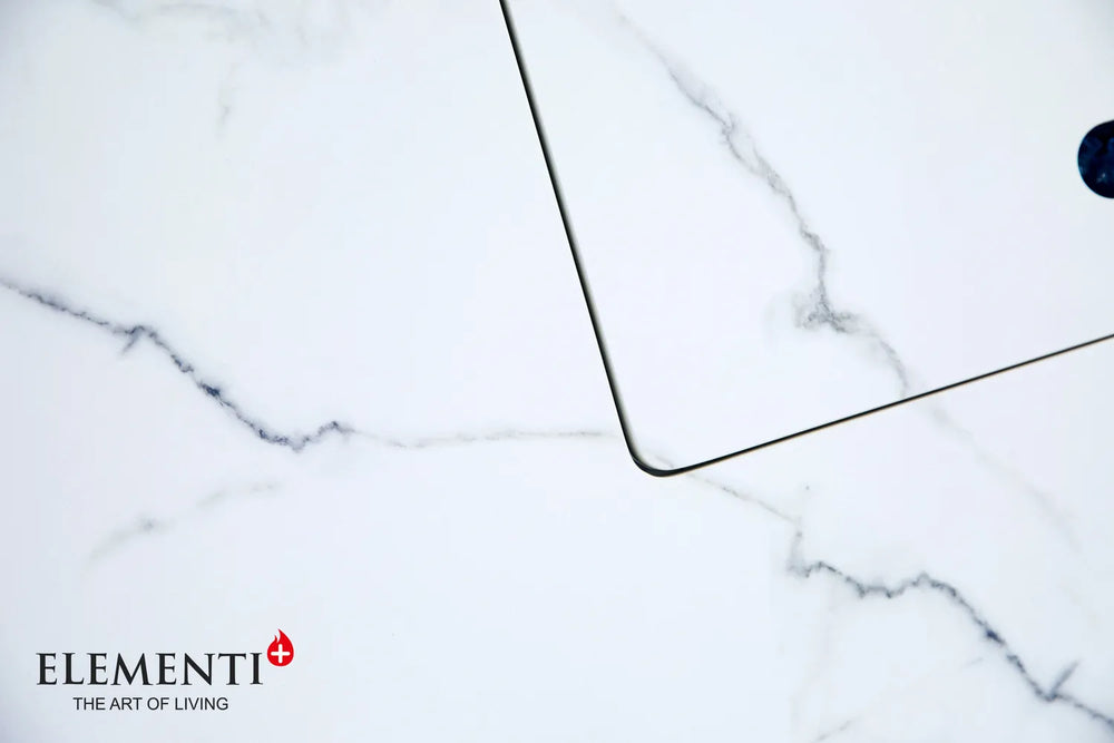 Close-up of the Elementi Plus Bianco fire table's clear tempered glass wind guard protecting a linear flame over blue fire glass.